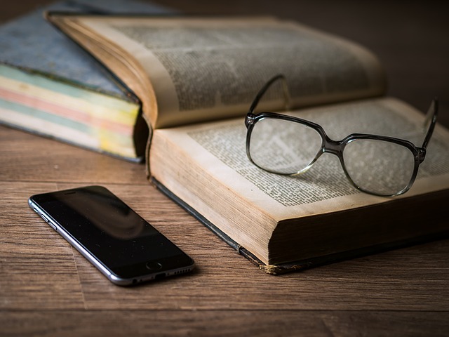 Nyitott könyv multifokális szemüveglencsével ellátott szemüveggel, mellette telefonnal.