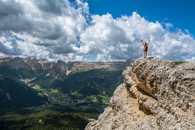Egy többfokális szemüveglencsés férfi felemelt karral áll a hegy tetején.
