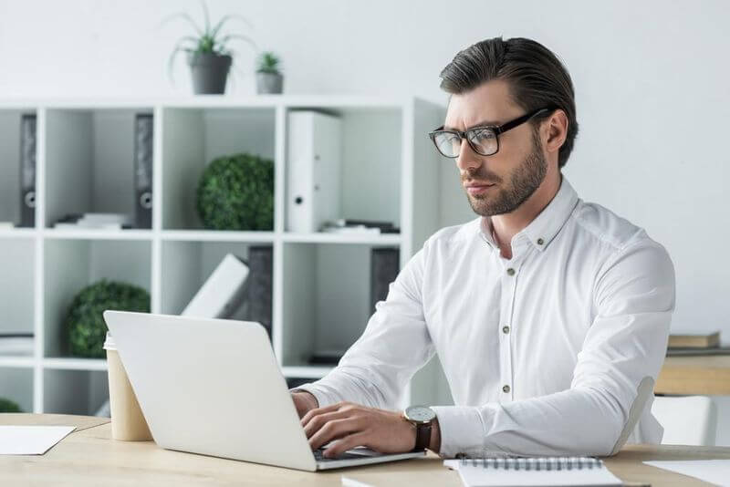 Egy férfi az iróasztalnál dolgozik a laptopján, szemüveget visel